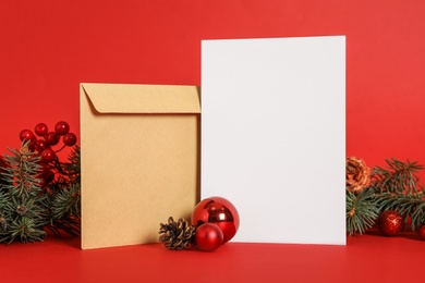 Blank greeting card, envelope and Christmas decor on red background, space for text