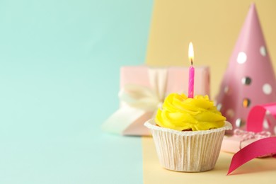 Tasty birthday cupcake with candle, gift box and party hat on colorful background. Space for text