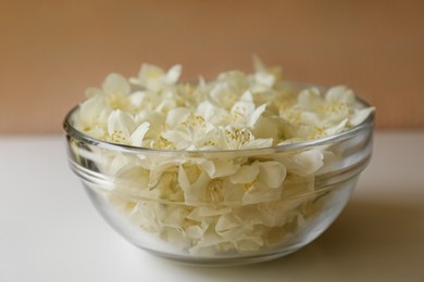Beautiful jasmine flowers in glass bowl on white table, closeup