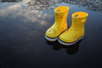 Yellow rubber boots in puddle outdoors, space for text. Autumn walk