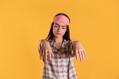 Young woman wearing pajamas and mask in sleepwalking state on yellow background