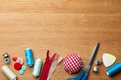 Photo of Flat lay composition with spools of threads and sewing tools on wooden table. Space for text