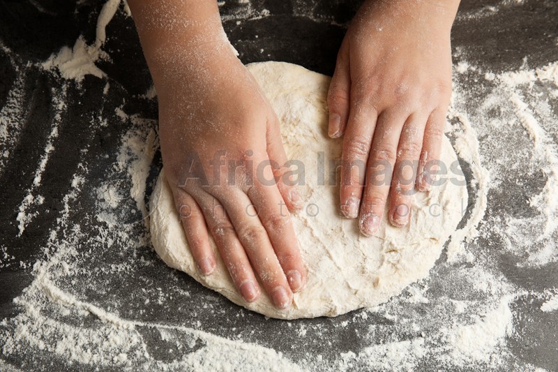 Woman kneading dough for pizza at grey table, closeup
