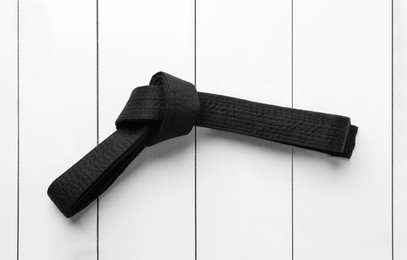Tied black belt on white wooden background, top view. Oriental martial arts