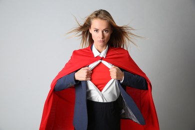 Confident businesswoman wearing superhero costume under suit on light grey background
