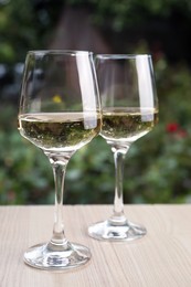Photo of Glasses of white wine served on wooden table outdoors