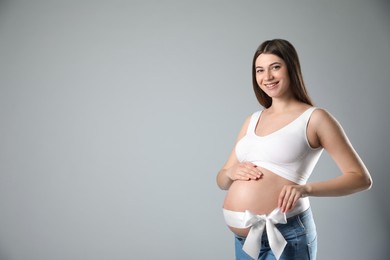 Photo of Young pregnant woman with bow on her belly against grey background, space for text. Time to give birth