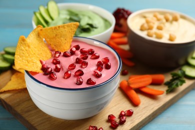 Bowl of delicious pink hummus with tortilla chips and pomegranate seeds on light blue wooden table