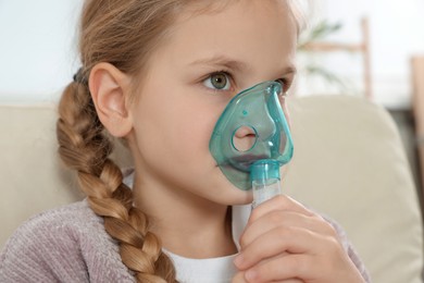 Photo of Little girl using nebulizer for inhalation indoors, closeup
