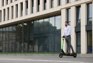 Businessman riding modern kick scooter on city street, space for text