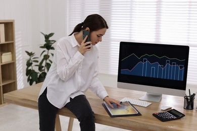 Businesswoman talking on phone while working in office. Forex trading