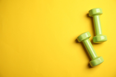 Top view of modern green dumbbells on yellow background, space for text. Physical fitness