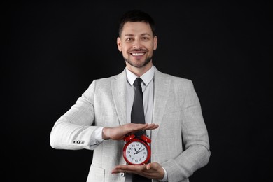 Happy businessman holding alarm clock on black background. Time management