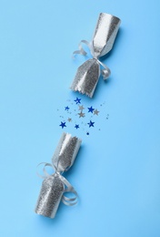 Open silver Christmas cracker with shiny confetti on light blue background, top view