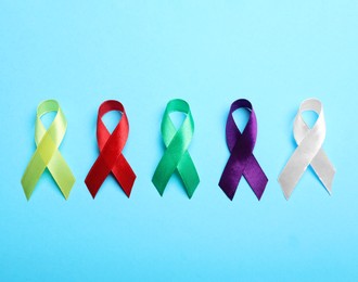 Colorful ribbons on light blue background, flat lay. World Cancer Day
