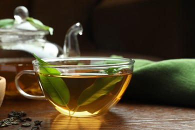Fresh green tea in glass cup with leaves on wooden table
