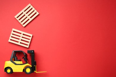 Toy forklift and wooden pallets on red background, flat lay. Space for text