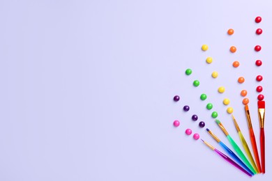 Photo of Creative flat lay composition with paint brushes and colorful candies on light grey background. Space for text