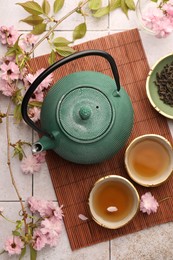 Photo of Traditional ceremony. Cup of brewed tea, teapot, dried leaves and sakura flowers on tiled table, flat lay