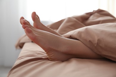 Person in bed with brown linens at home, closeup on feet