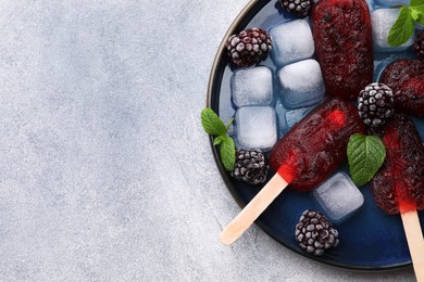 Plate of tasty blackberry ice pops and space for text on light grey table, top view. Fruit popsicle