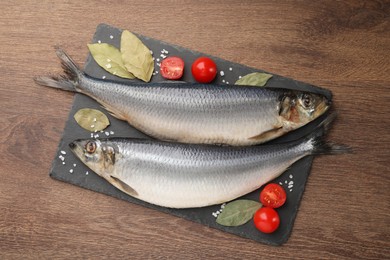 Photo of Slate plate with salted herrings, bay leaves and cherry tomatoes on wooden table, top view