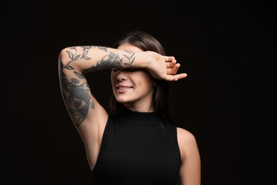 Photo of Beautiful woman with tattoos on arm against black background