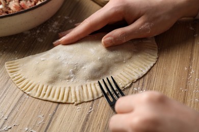Photo of Woman making chebureki with tasty filling at wooden table, closeup