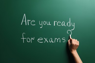 Woman writing phrase Are You Ready For Exams on green chalkboard, closeup