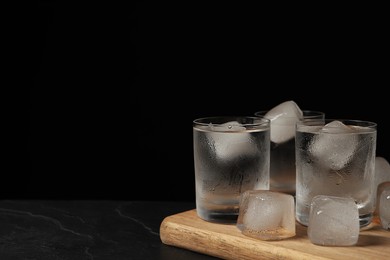 Shot glasses of vodka with ice cubes on black textured table. Space for text