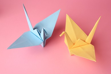 Photo of Origami art. Colorful handmade paper cranes on pink background, above view