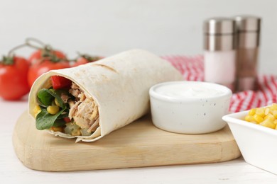 Photo of Delicious tortilla wrap with tuna and sauce on white wooden table