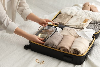 Photo of Woman packing suitcase for trip on bed, closeup