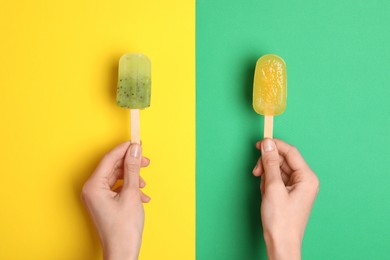 Woman holding delicious ice pops on color background, top view. Fruit popsicle