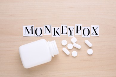 Word Monkeypox made of paper letters and bottle of pills on wooden table, flat lay