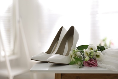 Pair of white high heel shoes, flowers and wedding dress on table indoors
