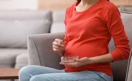 Young pregnant woman smoking cigarette at home, closeup. Space for text