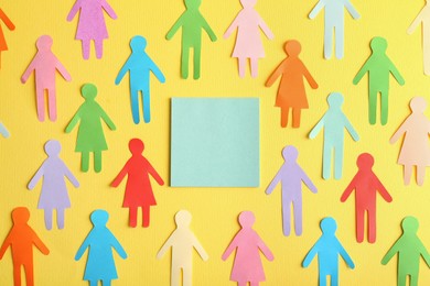 Photo of Many different paper human figures around blank card on yellow background, flat lay with space for text. Diversity and inclusion concept