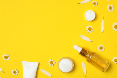 Flat lay composition with chamomiles and cosmetic products on yellow background. Space for text