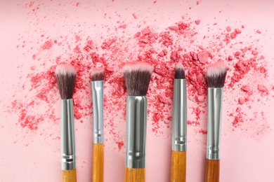 Makeup brushes and scattered eye shadow on pink background, flat lay
