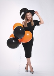 Beautiful woman in witch costume with balloons on white background. Halloween party