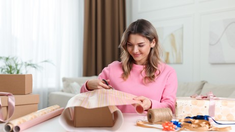 Beautiful young woman wrapping gift at table in living room