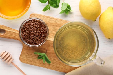 Cup of aromatic buckwheat tea, granules, lemons, mint and honey on white wooden table, flat lay