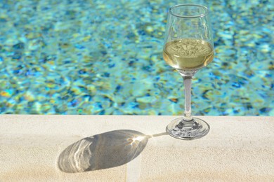 Photo of Glass of tasty wine on swimming pool edge, space for text
