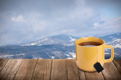 Cup of hot tea on wooden table and beautiful winter landscape on background