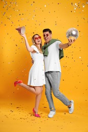 Happy couple with disco ball and confetti on yellow background