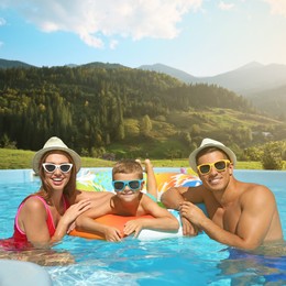 Happy family in outdoor swimming pool at luxury resort and beautiful view of mountains on sunny day