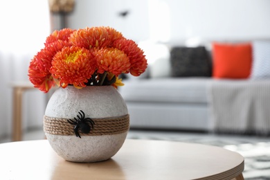 Beautiful flowers in vase with toy spider on table. Halloween interior decor