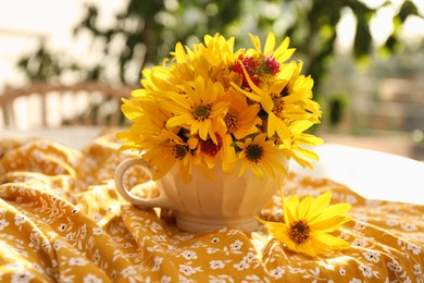 Beautiful bright yellow flowers in cup on fabric indoors