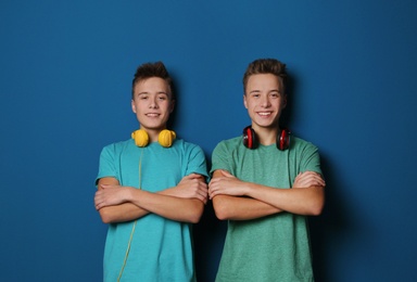 Teenage twin brothers with headphones on color background